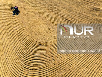 A worker dries rice at a sun-drying farm in Suqian, Jiangsu province, China, on October 2, 2024. (