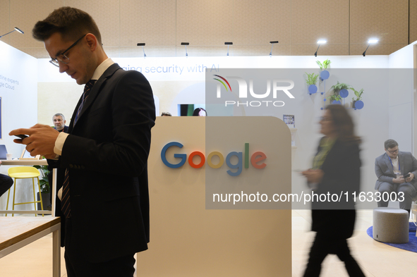 A man uses his smartphone and a woman walks past a Google stand during the Warsaw Security Forum 2024 in Warsaw, Poland on October 2, 2024....