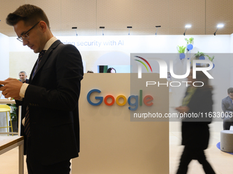 A man uses his smartphone and a woman walks past a Google stand during the Warsaw Security Forum 2024 in Warsaw, Poland on October 2, 2024....