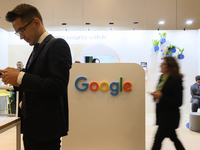 A man uses his smartphone and a woman walks past a Google stand during the Warsaw Security Forum 2024 in Warsaw, Poland on October 2, 2024....