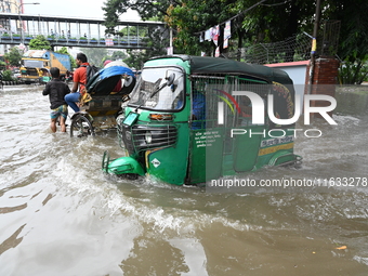 Vehicles and rickshaws try to drive with passengers through the waterlogged streets of Dhaka, Bangladesh, on October 3, 2024, after heavy mo...