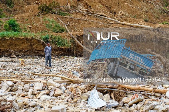 A man stands looking at his vehicle damaged by flooding from the Salamdo River in Patikharka, Kavrepalanchok District, Nepal, on October 3,...