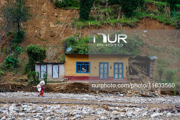 A woman walks in front of her home damaged by flooding from the Salamdo River in Patikharka, Kavrepalanchok District, Nepal, on October 3, 2...