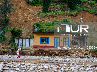 A woman walks in front of her home damaged by flooding from the Salamdo River in Patikharka, Kavrepalanchok District, Nepal, on October 3, 2...