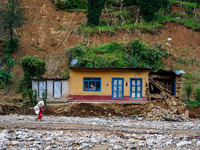 A woman walks in front of her home damaged by flooding from the Salamdo River in Patikharka, Kavrepalanchok District, Nepal, on October 3, 2...