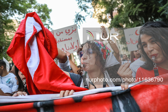 A young woman blows a whistle as she holds the national flag of Tunisia during a demonstration organized by the Tunisian Network for Rights...