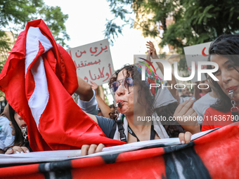 A young woman blows a whistle as she holds the national flag of Tunisia during a demonstration organized by the Tunisian Network for Rights...