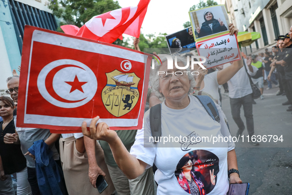 An elderly woman holds a placard bearing the national flag of Tunisia and the coat of arms of Tunisia during a demonstration organized by th...