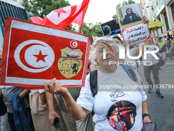 An elderly woman holds a placard bearing the national flag of Tunisia and the coat of arms of Tunisia during a demonstration organized by th...