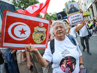 An elderly woman holds a placard bearing the national flag of Tunisia and the coat of arms of Tunisia during a demonstration organized by th...