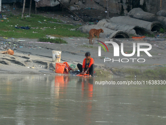 A woman living below the poverty line washes clothes in the Mahananda River in Siliguri, India, on October 5, 2024. River water pollution, d...