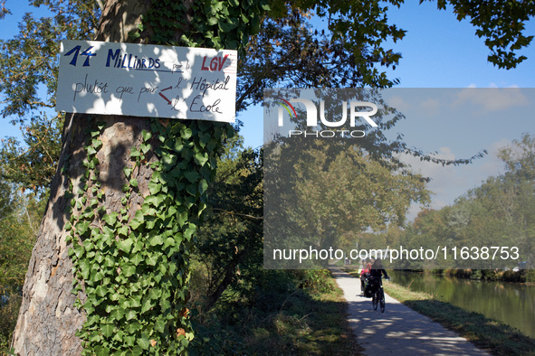 Cyclists ride on the Canal du Midi banks, and a placard reads 'EUR14 bn for the LGV rather than for education or hospitals'. Zadists, or dev...