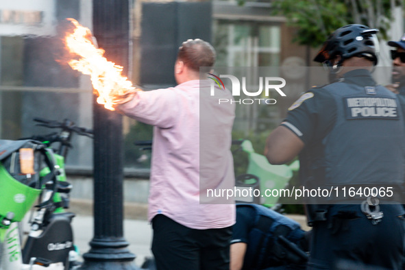 Police help a man who tried to set himself on fire as people demonstrate to mark one year of the war between Hamas and Israel in front of th...