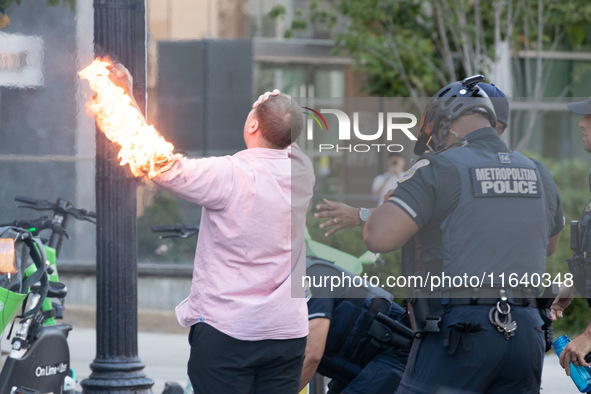 Police help a man who tried to set himself on fire as people demonstrate to mark one year of the war between Hamas and Israel in front of th...