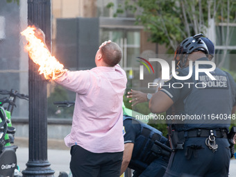 Police help a man who tried to set himself on fire as people demonstrate to mark one year of the war between Hamas and Israel in front of th...