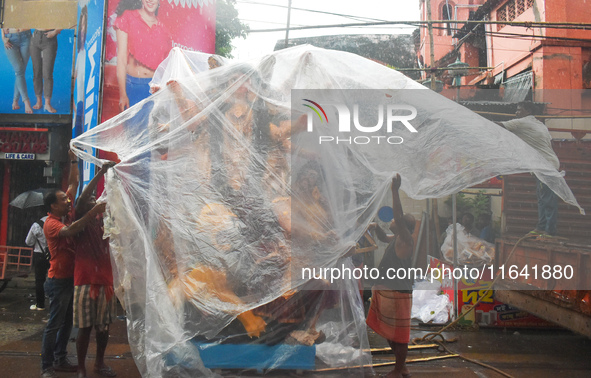 Laborers cover a Durga idol with plastic to protect it from rain on a truck for transport to a pandal, or a temporary platform, ahead of the...