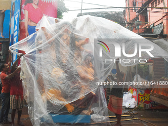 Laborers cover a Durga idol with plastic to protect it from rain on a truck for transport to a pandal, or a temporary platform, ahead of the...