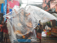 Laborers cover a Durga idol with plastic to protect it from rain on a truck for transport to a pandal, or a temporary platform, ahead of the...