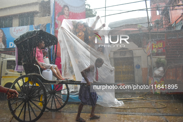 A hand-pulled rickshaw passes next to a Durga idol covered with plastic during rain in Kolkata, India, on October 6, 2024. 