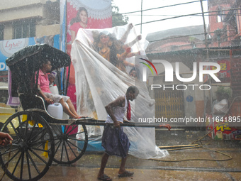 A hand-pulled rickshaw passes next to a Durga idol covered with plastic during rain in Kolkata, India, on October 6, 2024. (