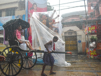 A hand-pulled rickshaw passes next to a Durga idol covered with plastic during rain in Kolkata, India, on October 6, 2024. (