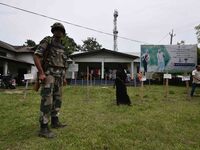 Indian security personnel stand guard as people wait in line to check their names on the draft list at the National Register of Citizens (NR...