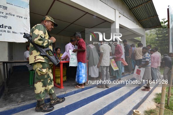 Indian security personnel stand guard as people wait in line to check their names on the draft list at the National Register of Citizens (NR...