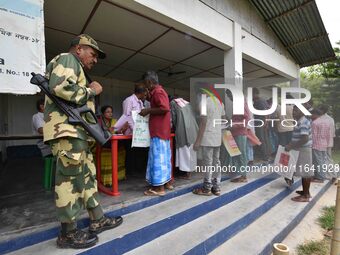 Indian security personnel stand guard as people wait in line to check their names on the draft list at the National Register of Citizens (NR...