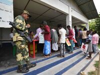 Indian security personnel stand guard as people wait in line to check their names on the draft list at the National Register of Citizens (NR...