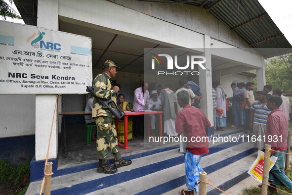 Indian security personnel stand guard as people wait in line to check their names on the draft list at the National Register of Citizens (NR...