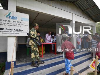 Indian security personnel stand guard as people wait in line to check their names on the draft list at the National Register of Citizens (NR...