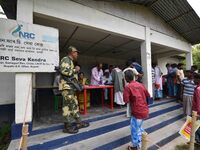 Indian security personnel stand guard as people wait in line to check their names on the draft list at the National Register of Citizens (NR...