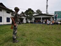 Indian security personnel stand guard as people wait in line to check their names on the draft list at the National Register of Citizens (NR...