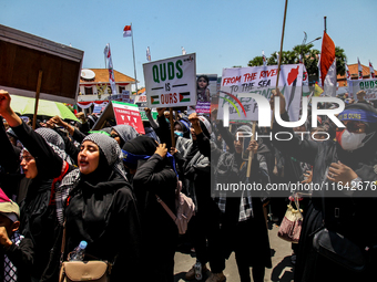 Muslims hold up posters during a pro-Palestinian rally on the eve of the one-year anniversary of the Israel-Hamas conflict in Surabaya, Indo...