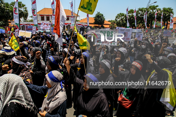 Muslims hold up posters during a pro-Palestinian rally on the eve of the one-year anniversary of the Israel-Hamas conflict in Surabaya, Indo...