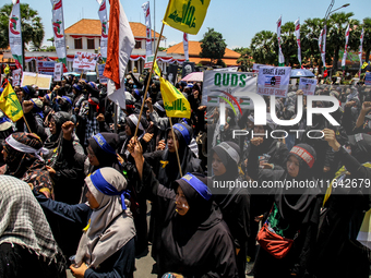 Muslims hold up posters during a pro-Palestinian rally on the eve of the one-year anniversary of the Israel-Hamas conflict in Surabaya, Indo...