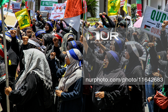 Muslims hold up posters during a pro-Palestinian rally on the eve of the one-year anniversary of the Israel-Hamas conflict in Surabaya, Indo...