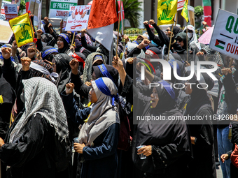 Muslims hold up posters during a pro-Palestinian rally on the eve of the one-year anniversary of the Israel-Hamas conflict in Surabaya, Indo...