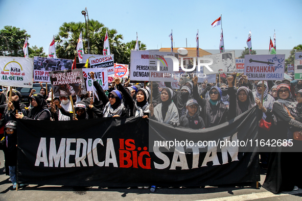 Muslims hold up posters during a pro-Palestinian rally on the eve of the one-year anniversary of the Israel-Hamas conflict in Surabaya, Indo...