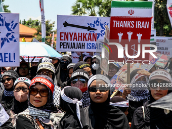 Muslims hold up posters during a pro-Palestinian rally on the eve of the one-year anniversary of the Israel-Hamas conflict in Surabaya, Indo...