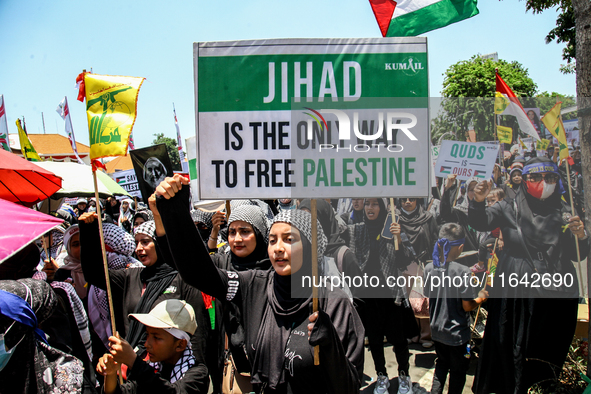 Muslims hold up posters during a pro-Palestinian rally on the eve of the one-year anniversary of the Israel-Hamas conflict in Surabaya, Indo...