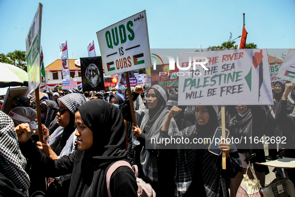 Muslims hold up posters during a pro-Palestinian rally on the eve of the one-year anniversary of the Israel-Hamas conflict in Surabaya, Indo...