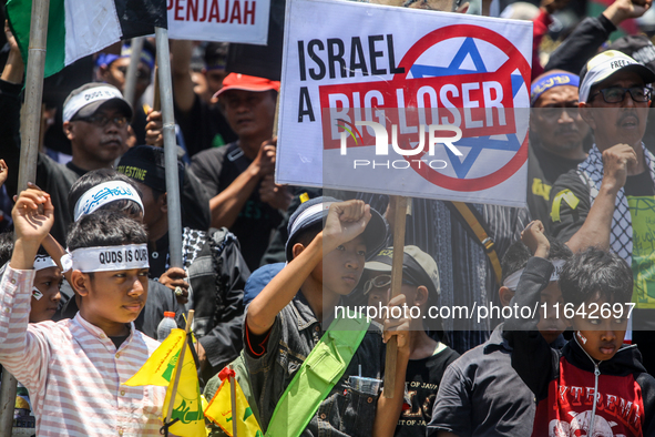 Muslims hold up posters during a pro-Palestinian rally on the eve of the one-year anniversary of the Israel-Hamas conflict in Surabaya, Indo...