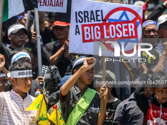 Muslims hold up posters during a pro-Palestinian rally on the eve of the one-year anniversary of the Israel-Hamas conflict in Surabaya, Indo...