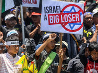 Muslims hold up posters during a pro-Palestinian rally on the eve of the one-year anniversary of the Israel-Hamas conflict in Surabaya, Indo...