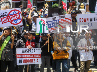 Muslims hold up posters during a pro-Palestinian rally on the eve of the one-year anniversary of the Israel-Hamas conflict in Surabaya, Indo...