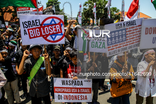 Muslims hold up posters during a pro-Palestinian rally on the eve of the one-year anniversary of the Israel-Hamas conflict in Surabaya, Indo...