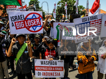 Muslims hold up posters during a pro-Palestinian rally on the eve of the one-year anniversary of the Israel-Hamas conflict in Surabaya, Indo...