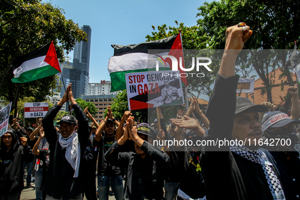 Muslims hold up posters during a pro-Palestinian rally on the eve of the one-year anniversary of the Israel-Hamas conflict in Surabaya, Indo...