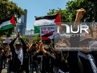 Muslims hold up posters during a pro-Palestinian rally on the eve of the one-year anniversary of the Israel-Hamas conflict in Surabaya, Indo...